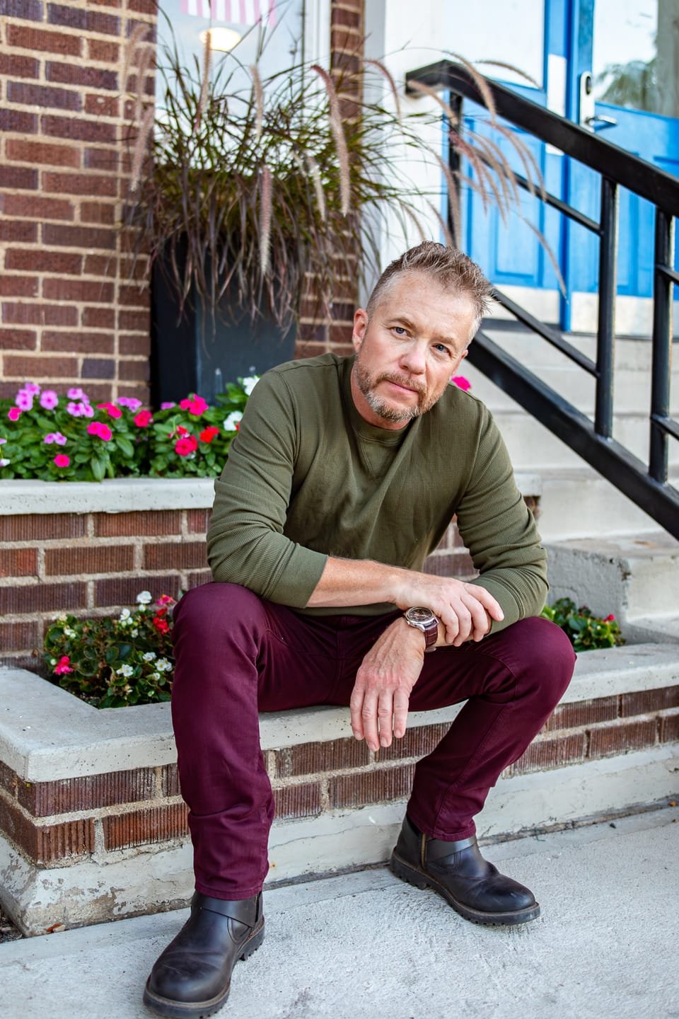 Cecil Hawthorne sitting on brick steps beside a planter of flowers, in an olive henley.